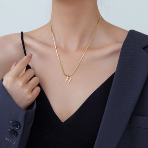 Golden H-pendant necklace on snake chain shown on a female model with blazer