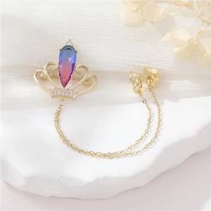 Crown brooch with blue teardrop zircon and gold chains on a white stone base