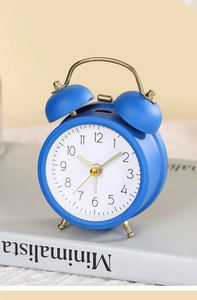 Close-up of blue twin bell alarm clock with golden metal hands on a white book