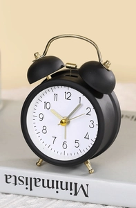 Close-up of a matte black vintage twin bell alarm clock with gold hands on a white book