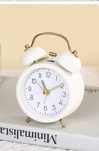 Detailed close-up of a white twin-bell minimalist metal alarm clock on grey books