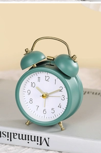 Close-up of a teal metal twin bell alarm clock on a minimalist book with golden accents