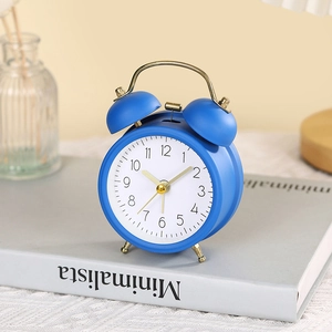 Minimalist blue metal twin bell alarm clock with gold accents on a book surface