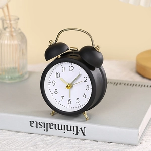 Minimalist black twin bell metal alarm clock with gold accents on a bookshelf