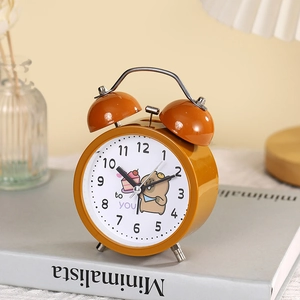Retro orange metal twin bell alarm clock with cute cartoon bear on desktop