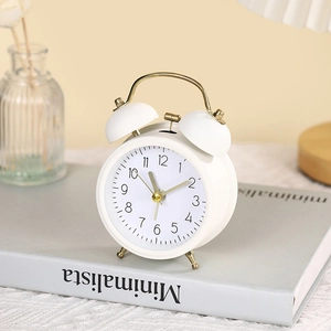 Classic white twin bell alarm clock with gold metal accents on a minimalist book