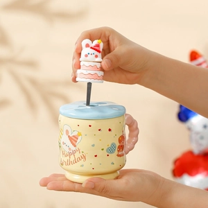 Close-up of yellow ceramic Capybara mug with pink wavy handle and blue lid and spoon