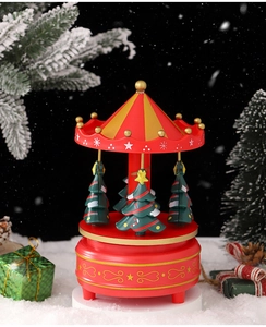 Close-up of a festive red Christmas tree carousel music box on a snowy background