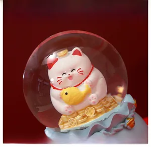 Detail view of Maneki Neko glass ball with white lucky cat and golden coins on wave base