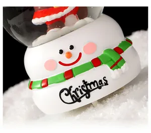 Détail de la base de boule à neige avec bonhomme de neige en résine et texte de Noël