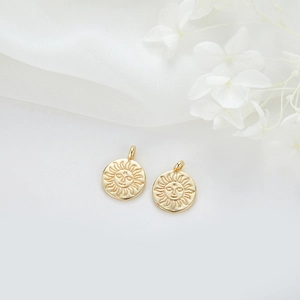 Détail de pendentifs soleil dorés avec visage en relief sur un tissu floral blanc