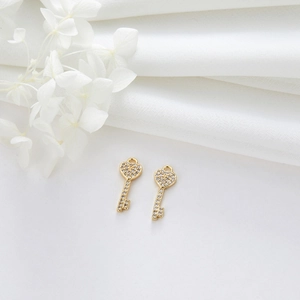 Detailed view of heart-shaped gold key pendants with white zircon pavé on white fabric