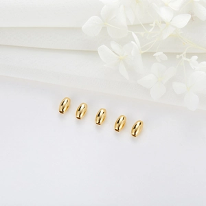 Five gold plated cylindrical beads for DIY jewelry making on white elegant fabric background