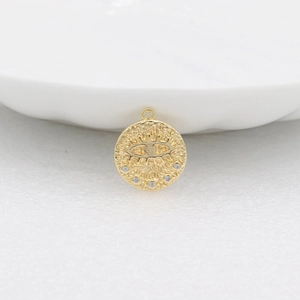 Gold-plated evil eye coin pendant with sun rays and zircon stones on white sand