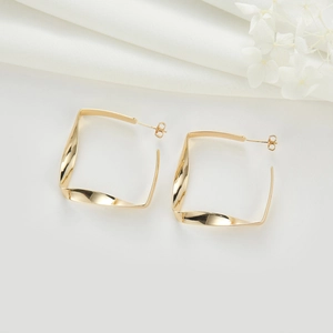 Boucles d'oreilles carrées torsadées dorées en forme de C sur fond de tissu blanc élégant