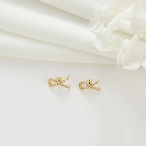 Detail of 14k gold-plated bow earrings set with white cubic zirconia on white linen