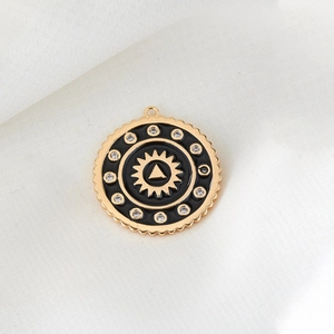 Detailed view of a circular gold-plated pendant with black enamel and zircon inlay