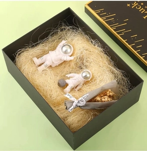 Gift box detail with astronaut figurines, raffia filler, and small dried flower bouquet