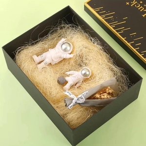 Astronaut figurines in a black gift box with raffia filler and dried flowers