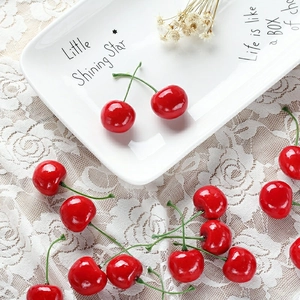 Artificial red cherries with stems on a white lace cloth and porcelain plate for decor