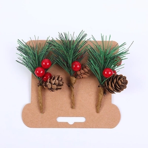 Tre rami decorativi natalizi con bacche rosse e pigne su cartoncino espositivo