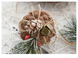 Close-up of pine cone hanging ornament with bells, red berries and snow-dusted needles