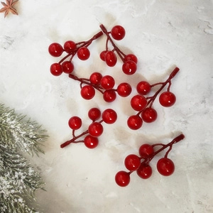 Five glossy red artificial berry stems with frosted pine needles on marble background