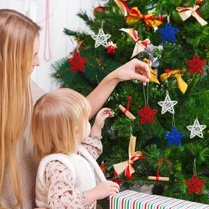 Close-up of red, white and blue woven star ornaments being hung on a tree by a mother