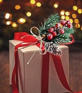 Close-up of a square gift box with red berries, pine needles, pinecone and red silk ribbon