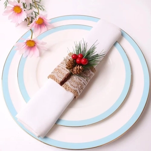 Close-up of burlap napkin ring with pine needles, red berries and lace on a white plate