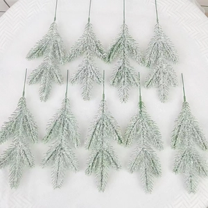 Flat lay macro of nine green artificial pine branches with heavy white snow flocking effect