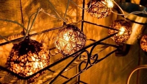Detail of warm LED rattan ball string lights hanging on a metal rack for cozy home decor