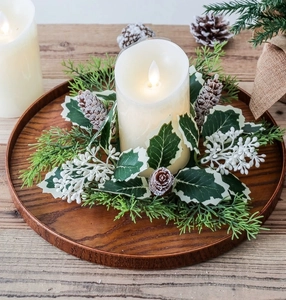 Close-up of a Christmas candle ring with pine cones, berries, and an LED candle on wood