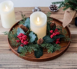 Detail of LED candle with red berry wreath and pine cones on a wooden tray