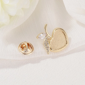 Elegant gold apple brooch with zircon leaves on a minimalist white fabric background