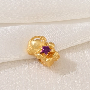 Macro shot of gold-plated astronaut charm with purple enamel star on white silk
