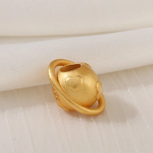Macro detail of S925 gold-plated Saturn charm with embossed heart on white fabric
