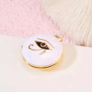 Colgante relicario dorado con Ojo de Horus y gema roja sobre arena rosa