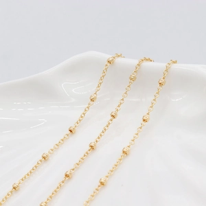 Minimalist 14K gold beaded chain necklace with frosted spheres on white ceramic plate