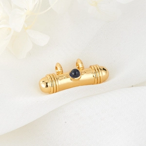 Golden cylindrical cow-pattern pendant with deep blue gemstone on white fabric
