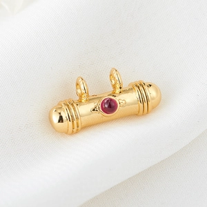 Detail view of golden cylindrical pendant with red cabochon stone and polished finish