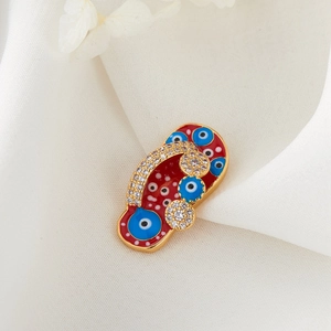 Close-up of golden flip-flop charm with red enamel and blue Evil Eye patterns