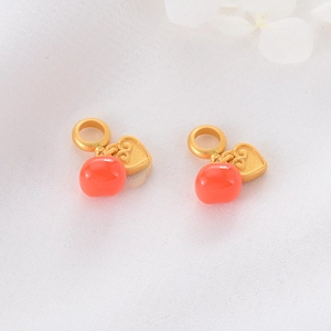 Detail of red bead persimmon charm with gold heart cloud pattern on white fabric