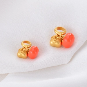 Macro detail of two gold persimmon charms with orange resin on white textured fabric