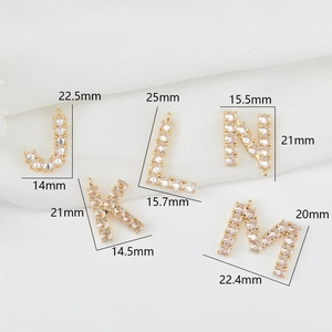 Macro-opname van vergulde J K L M N letterhangers met zirkoon voor DIY-sieraden