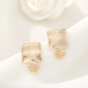 Detalle macro de aretes cuadrados de oro cepillado con colgantes de margaritas huecas