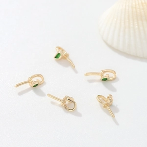 Detalle de pendientes dorados con hojas de esmalte verde sobre un fondo de concha blanca