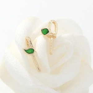 Primer plano de pendientes dorados con piedras preciosas verdes en forma de hoja elegante