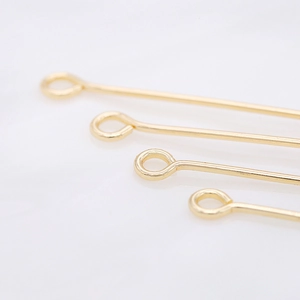 Macro shot of polished 14K gold-plated eye pins showing smooth rings and metallic texture