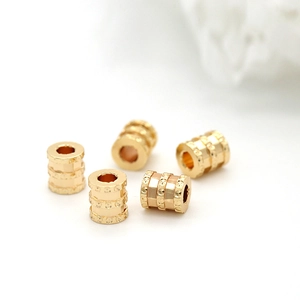Detailed macro shot of five gold plated copper cylindrical spacer beads with stripe patterns